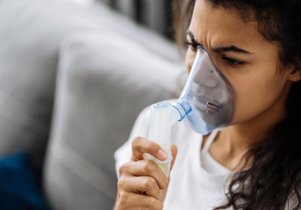 Close-up photo of a young african american woman putting on oxygen mask, having an asthma. Unhealthy girl suffer from serious viral illness, having illness, flu